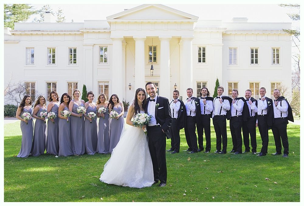 Bride and groom pose with wedding party in front of a white mansion with columns.