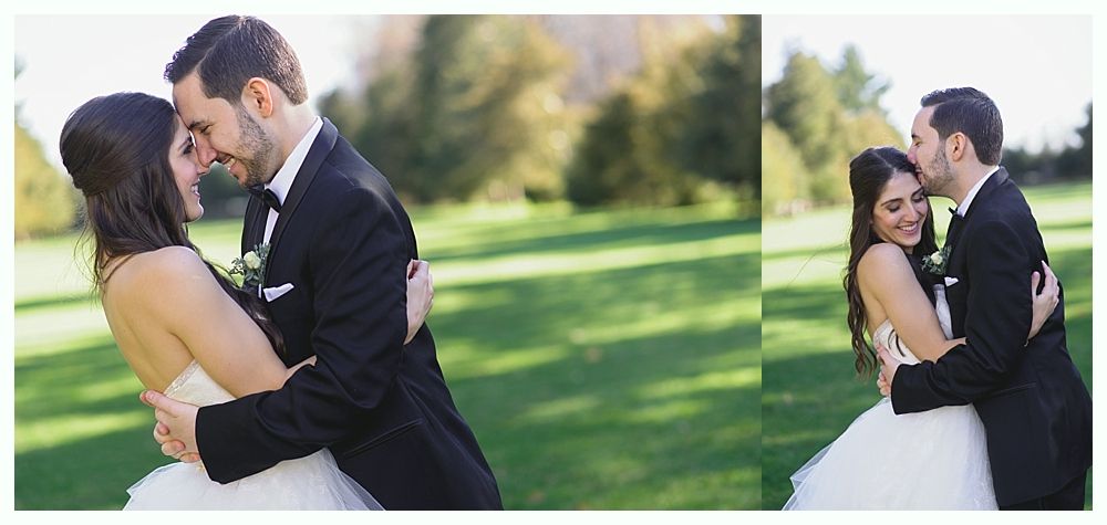 Wedding couple embraces outdoors on a grassy field; groom kisses bride's forehead.