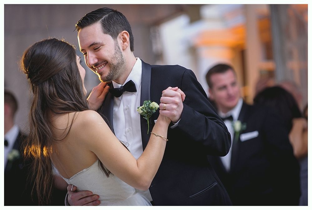 Couple dances close, man in tux smiles, woman in wedding dress.