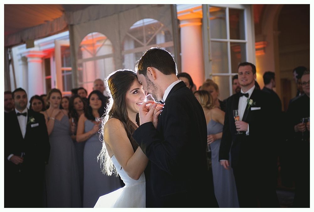 Bride and groom dancing at a wedding reception, guests watching in background.