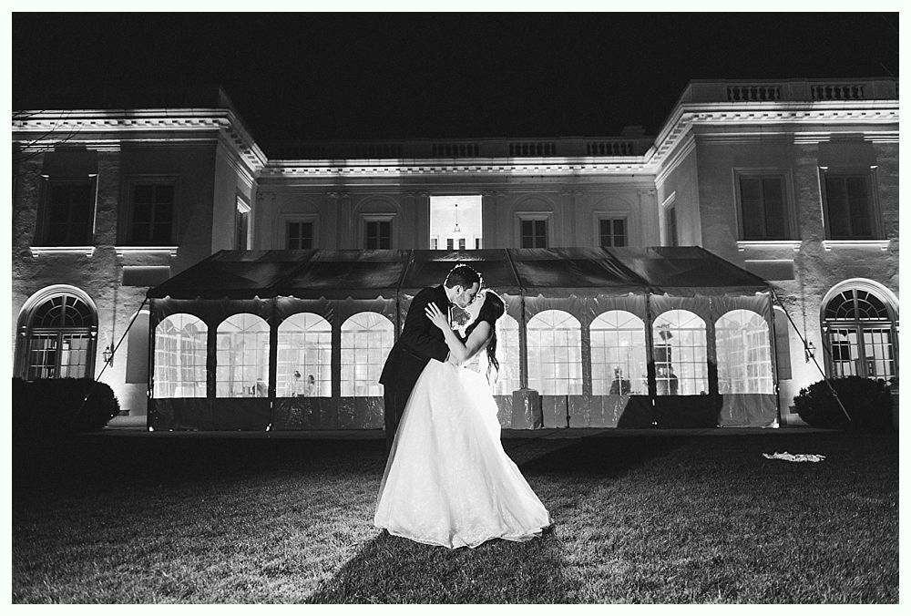 Couple embracing in front of a brightly lit building at night; woman in a wedding dress, man in a suit.