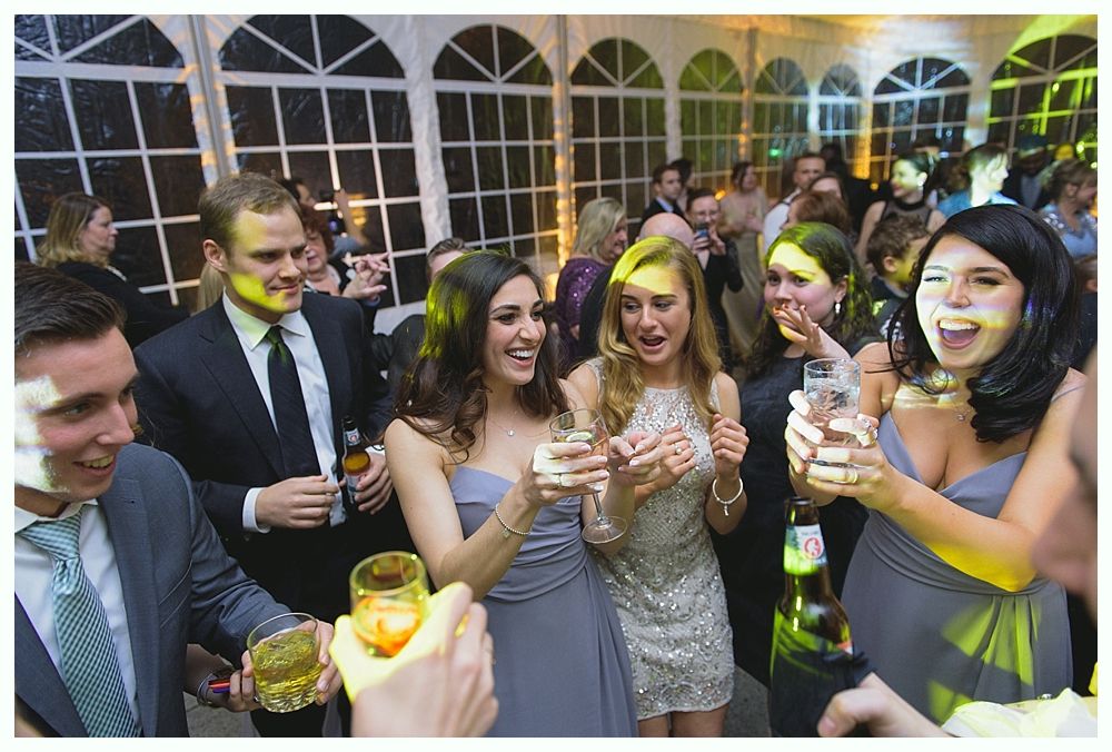 People toasting drinks at a celebration inside a well-lit tent. Many are smiling.