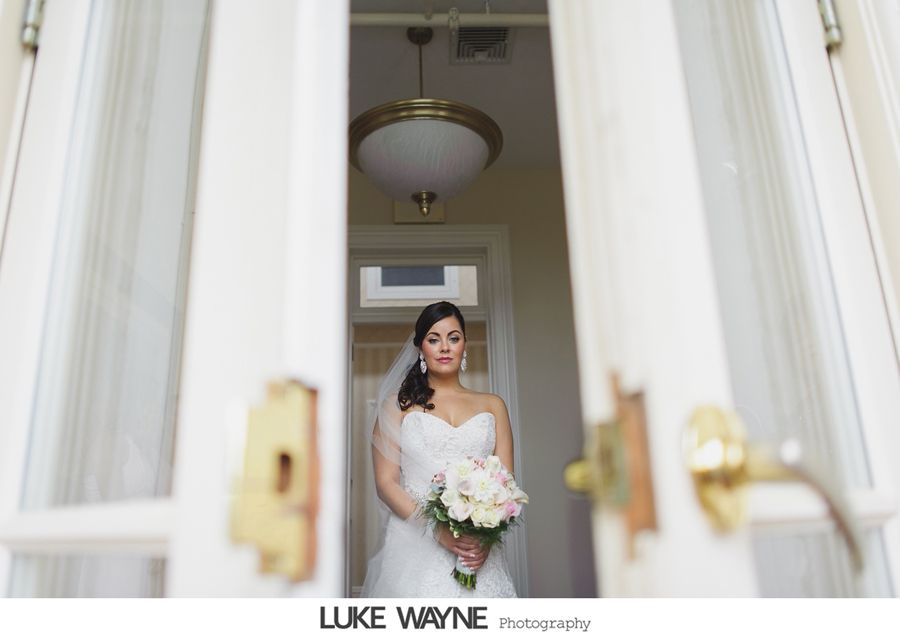 Bride in a white dress and veil holding flowers, framed by open white doors.