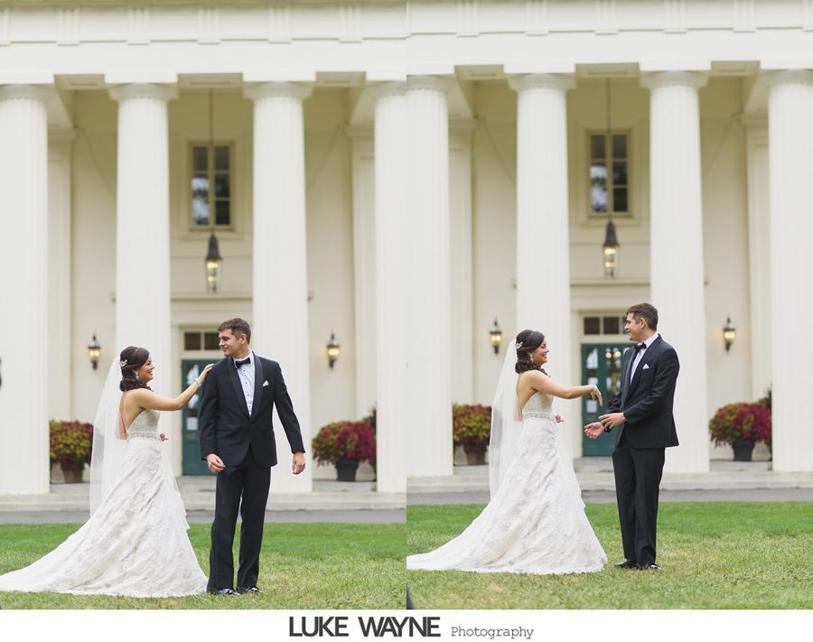 Bride and groom at a wedding, touching hands. They stand in front of a white building with pillars.