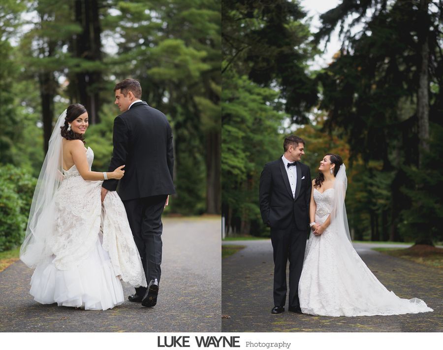 Bride and groom walk down a tree-lined path. She looks back smiling. He wears a suit. Romantic wedding day.