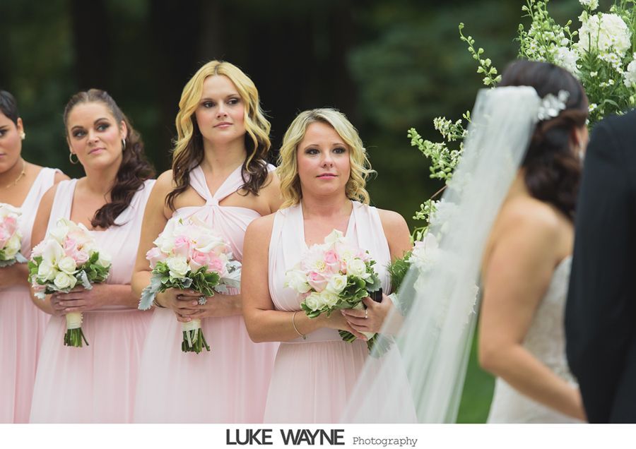 Bridesmaids in pink dresses watching the bride during an outdoor wedding ceremony.