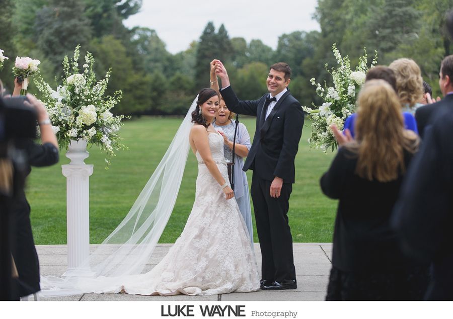 Newly married couple raises hands in celebration at outdoor wedding ceremony.