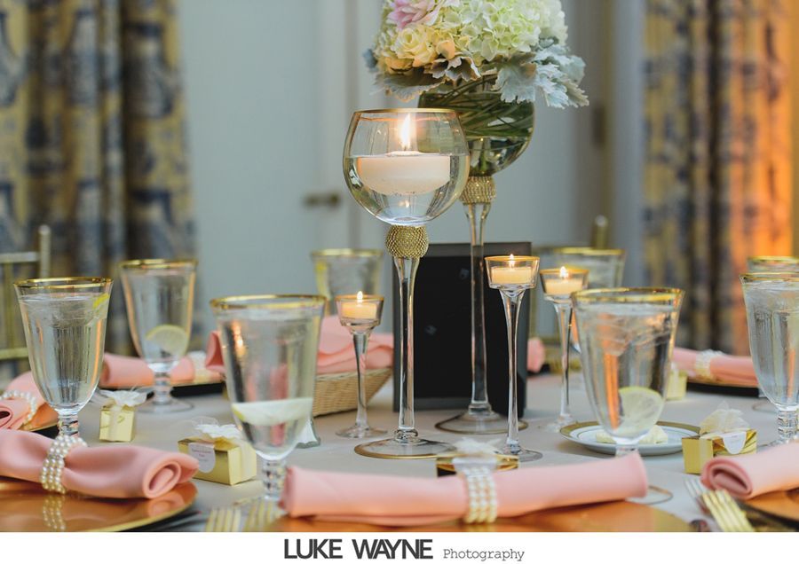 Elegant table setting with gold trim, pink napkins, candles, and floral centerpiece.