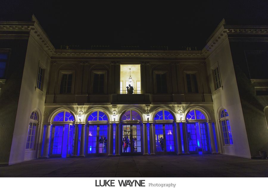Exterior of a building lit in blue at night. A couple is silhouetted in a window above the entrance.
