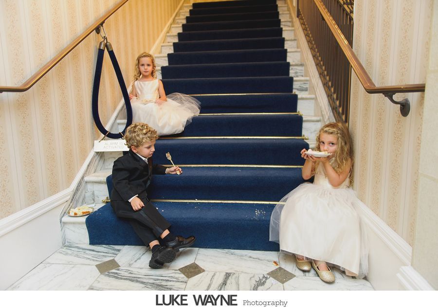 Children in formal wear playing on a staircase with a blue runner, eating cake.