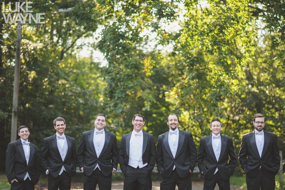 Couple poses at a rock face and arched stone doorway. Both wear denim jackets; woman in coral skirt.
