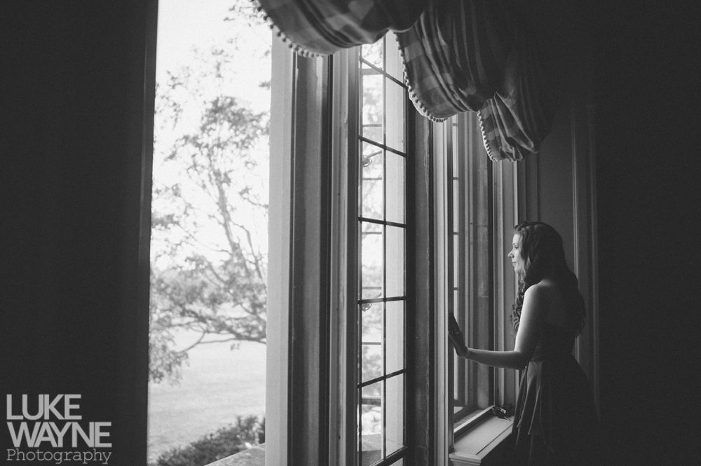 Couple embracing outdoors; woman smiles up at man, both in casual wear, near trees.