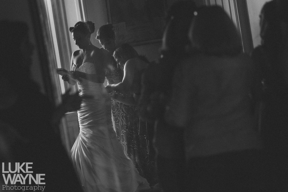 Couple embraces on a rocky outcrop, facing each other. Black and white photograph, cloudy sky, tree on the left.