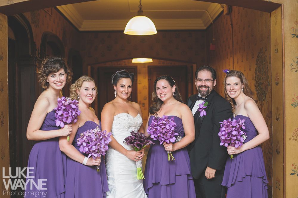 Couple embraces on a rocky hilltop, silhouetted tree, sunset, dramatic sky.