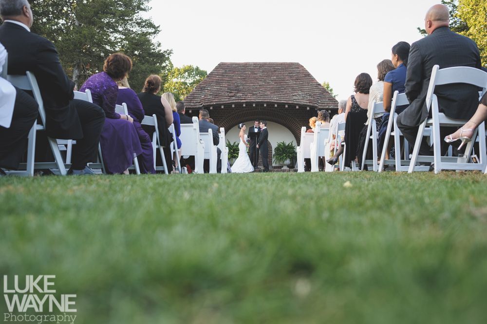 Couple embracing at sunset; man in green shirt, woman in denim jacket and red dress, with blowing hair.