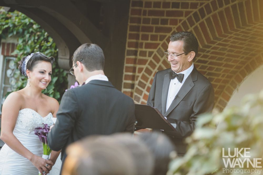 Couple embracing at sunset; man in green shirt, woman in denim jacket and red dress, with blowing hair.