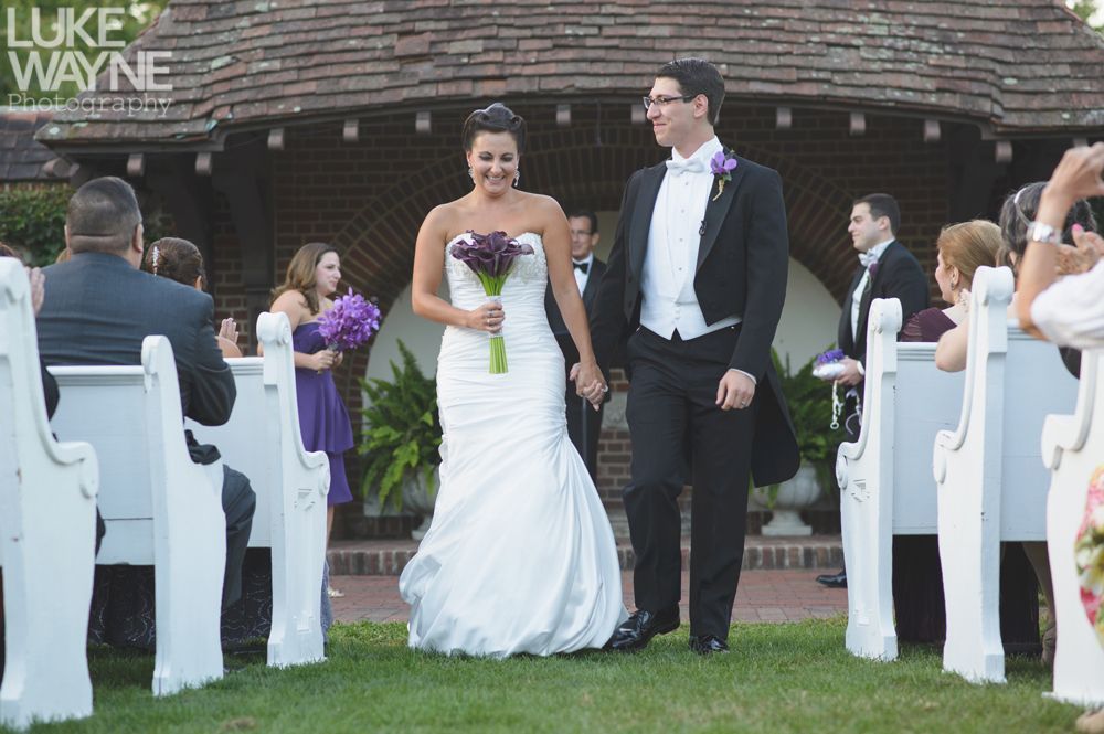Couple embracing at sunset; man in green shirt, woman in denim jacket and red dress, with blowing hair.