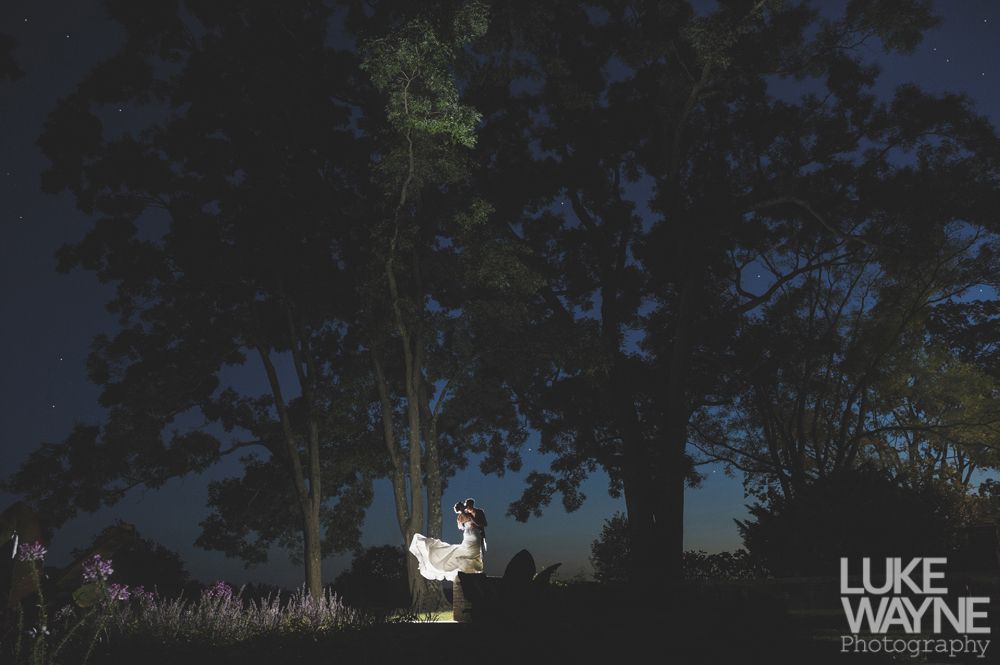 Couple embracing, woman smiling, man's arms around her. Black and white photo, outdoor setting.