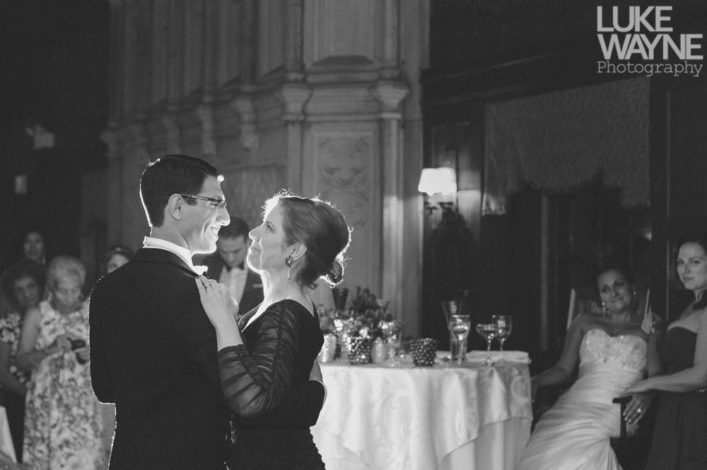 Couple embracing at sunset; man in green shirt, woman in denim jacket and red dress, with blowing hair.
