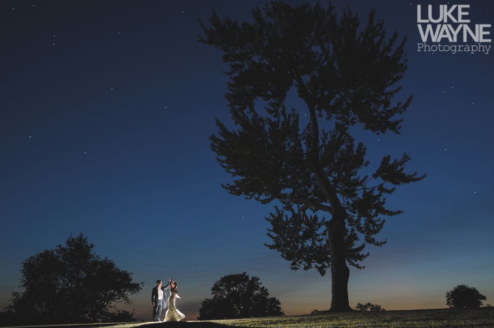 Couple embracing at sunset; man in green shirt, woman in denim jacket and red dress, with blowing hair.