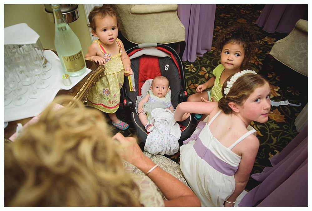 Bride in white gown holding bouquet, posed outdoors. Sunlight streams through trees.