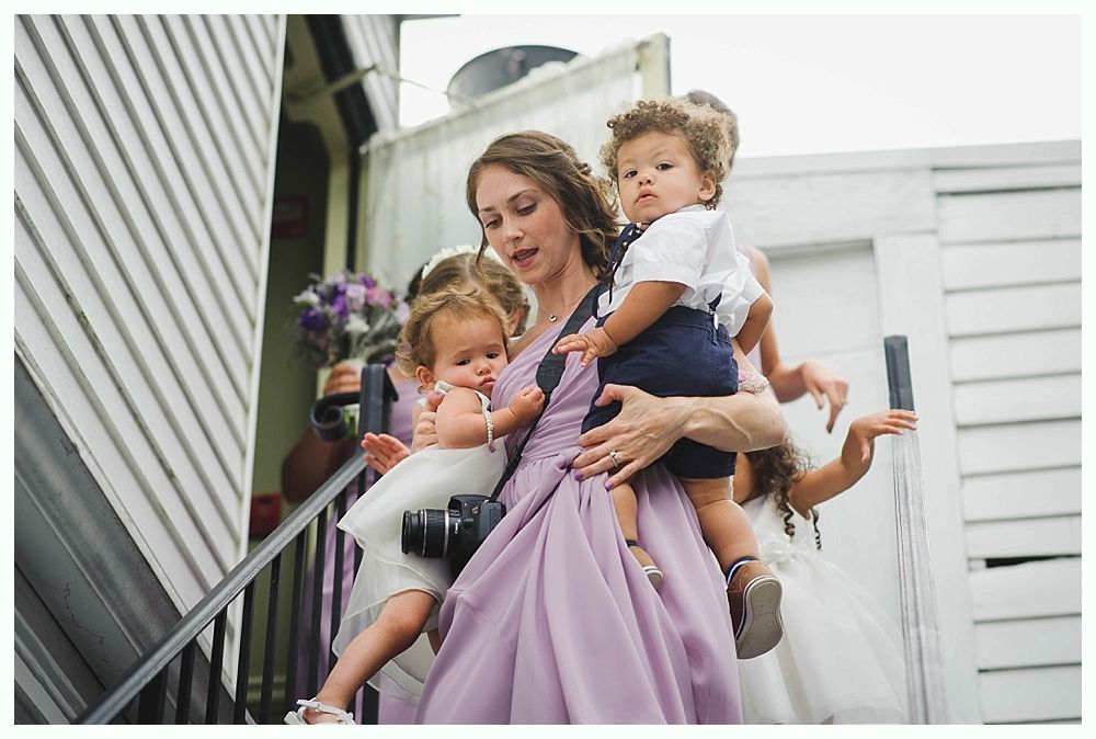 Bride with arms up, making a funny face, groom looking at his hand, cake cutting in background.