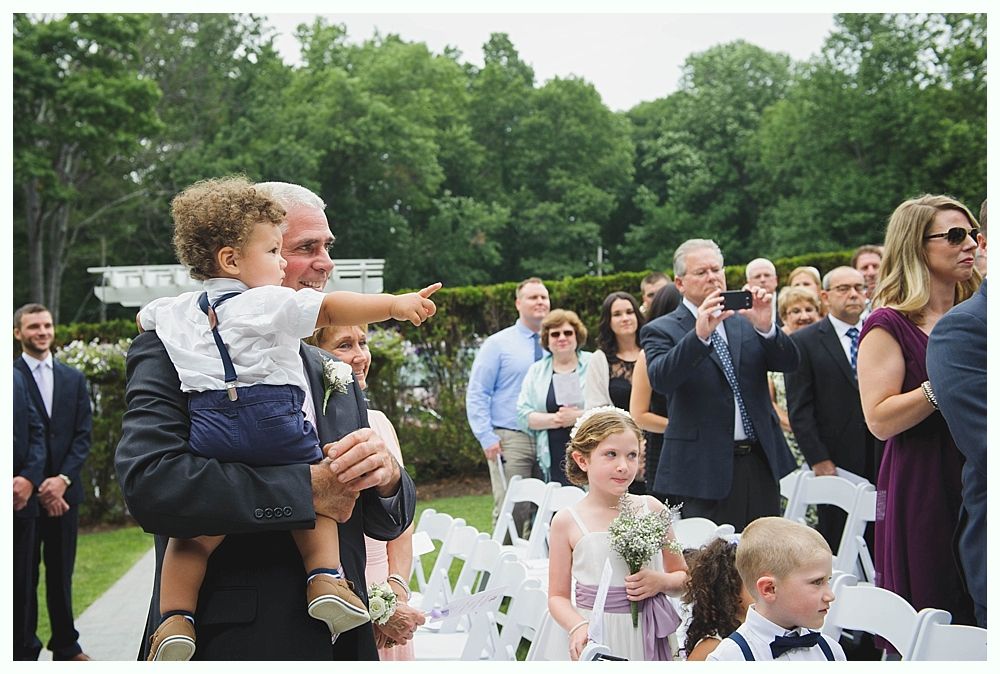 Bride with arms up, making a funny face, groom looking at his hand, cake cutting in background.