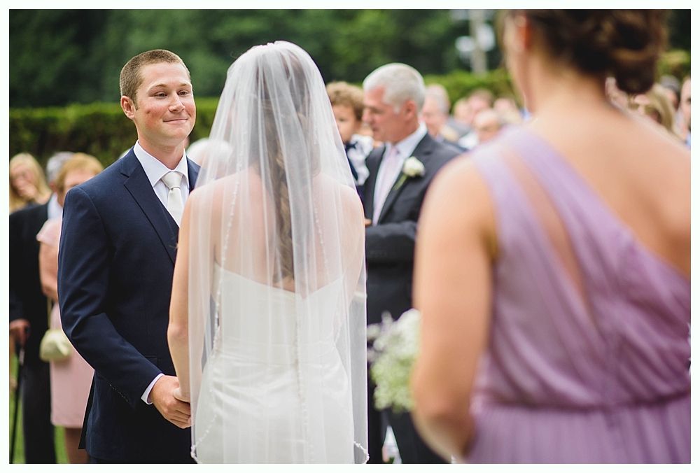 Bride with arms up, making a funny face, groom looking at his hand, cake cutting in background.