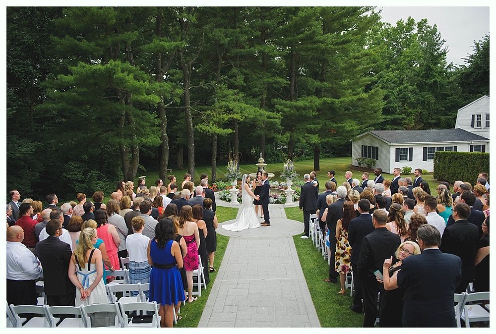 Bride with arms up, making a funny face, groom looking at his hand, cake cutting in background.