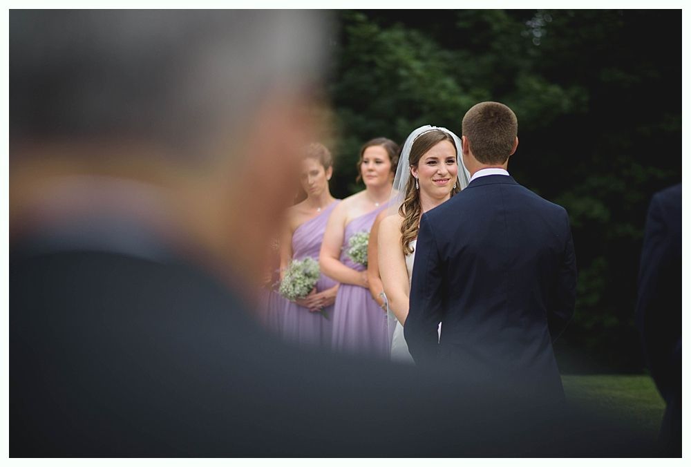 Bride with arms up, making a funny face, groom looking at his hand, cake cutting in background.