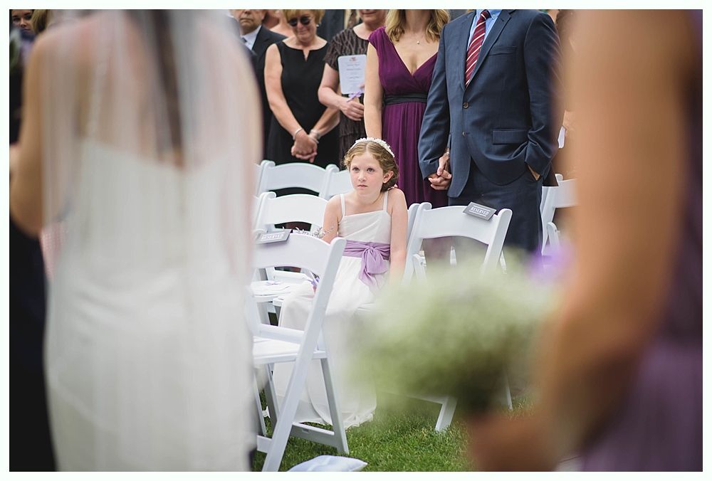 Bride with arms up, making a funny face, groom looking at his hand, cake cutting in background.