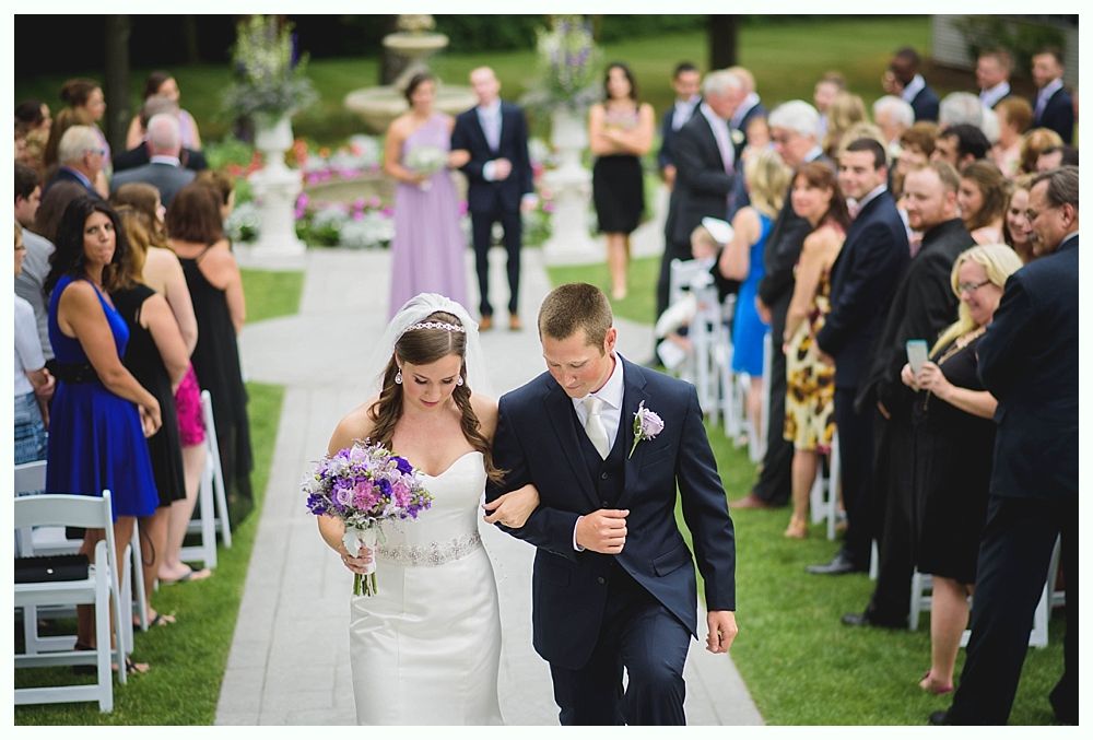Bride with arms up, making a funny face, groom looking at his hand, cake cutting in background.