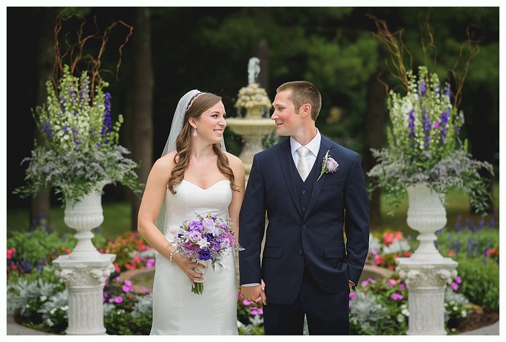 Bride with arms up, making a funny face, groom looking at his hand, cake cutting in background.