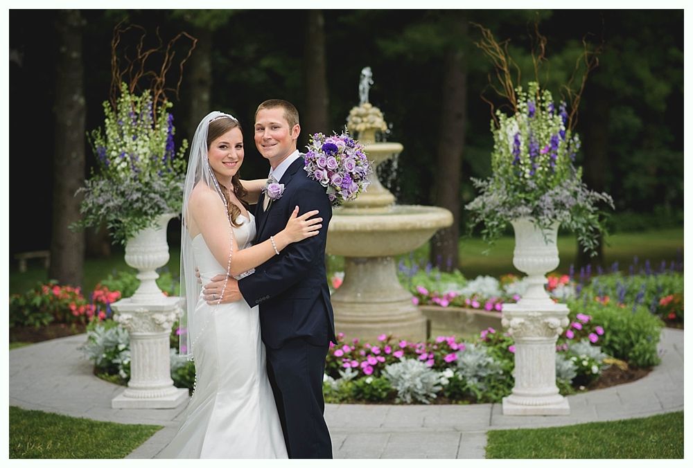 Bride with arms up, making a funny face, groom looking at his hand, cake cutting in background.