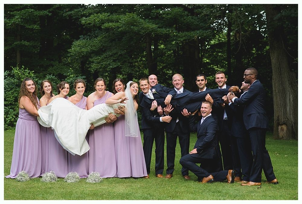 Bride with arms up, making a funny face, groom looking at his hand, cake cutting in background.