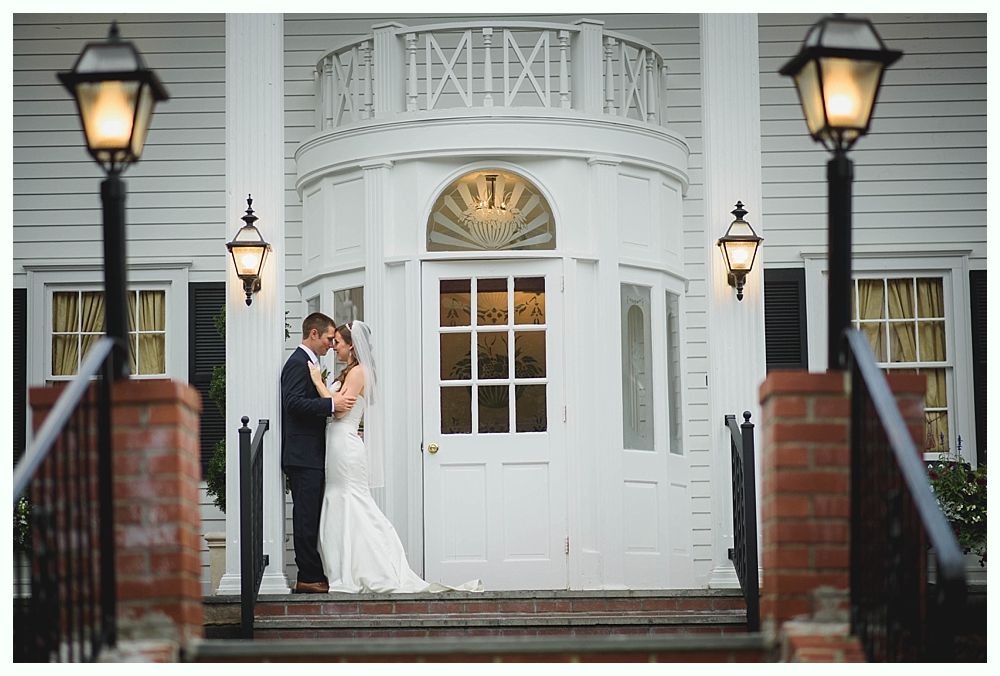 Bride with arms up, making a funny face, groom looking at his hand, cake cutting in background.