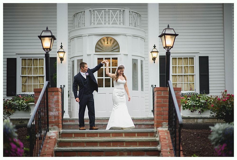 Bride with arms up, making a funny face, groom looking at his hand, cake cutting in background.