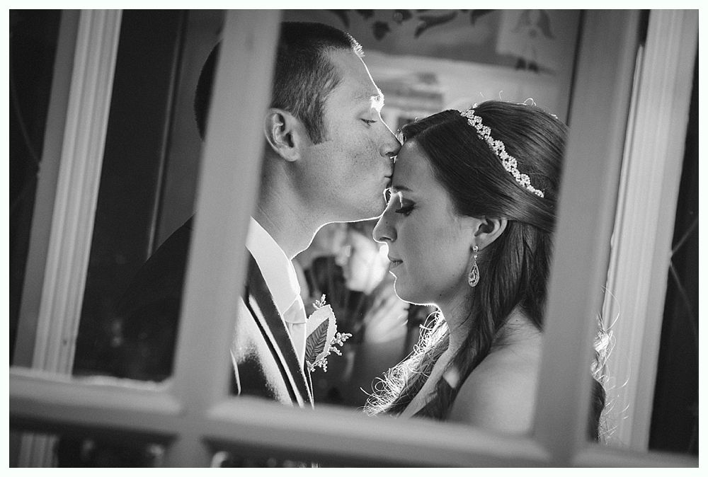 Bride with arms up, making a funny face, groom looking at his hand, cake cutting in background.
