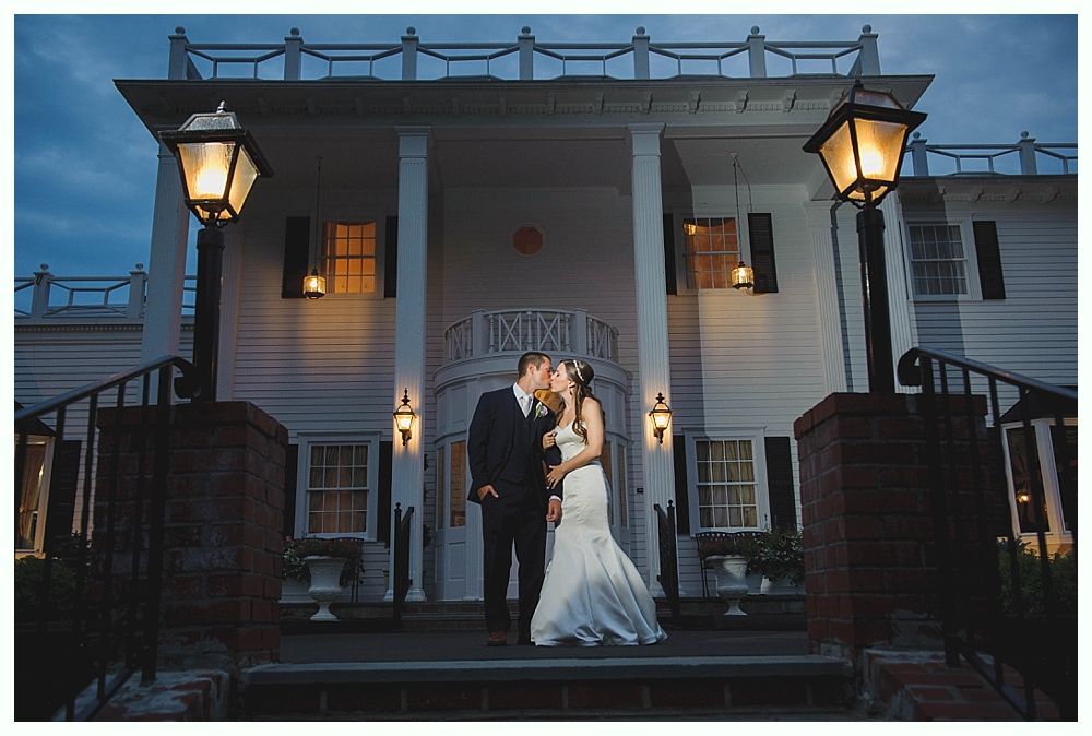 Bride with arms up, making a funny face, groom looking at his hand, cake cutting in background.
