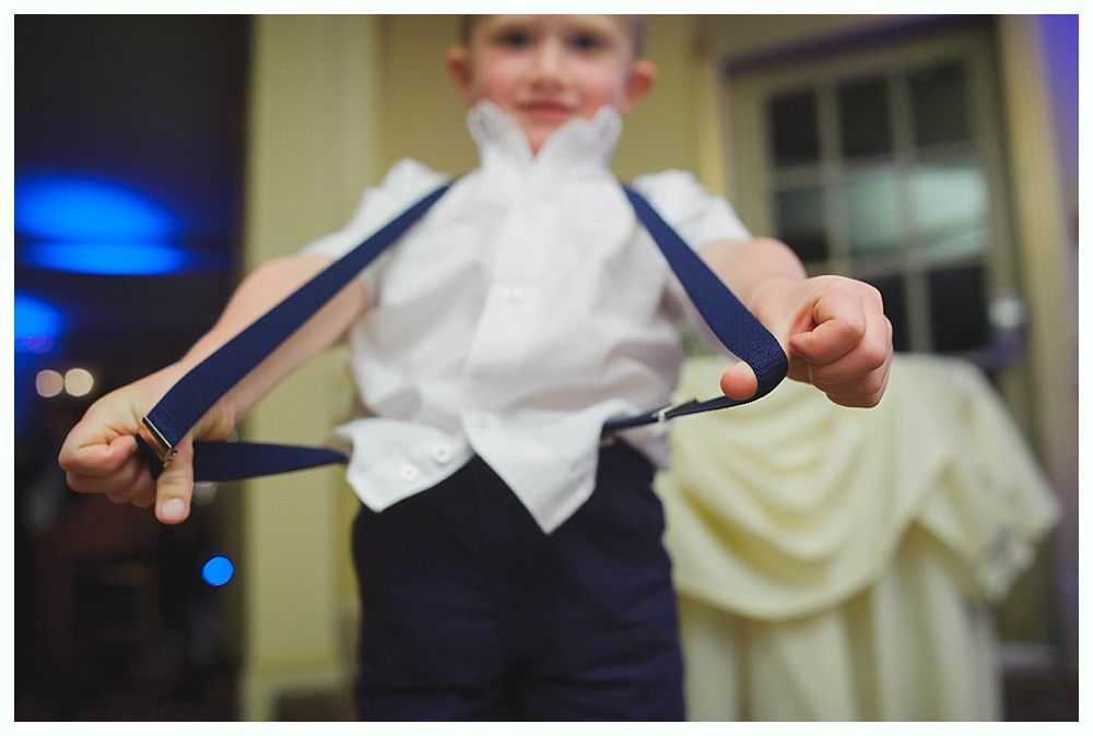 Bride with arms up, making a funny face, groom looking at his hand, cake cutting in background.