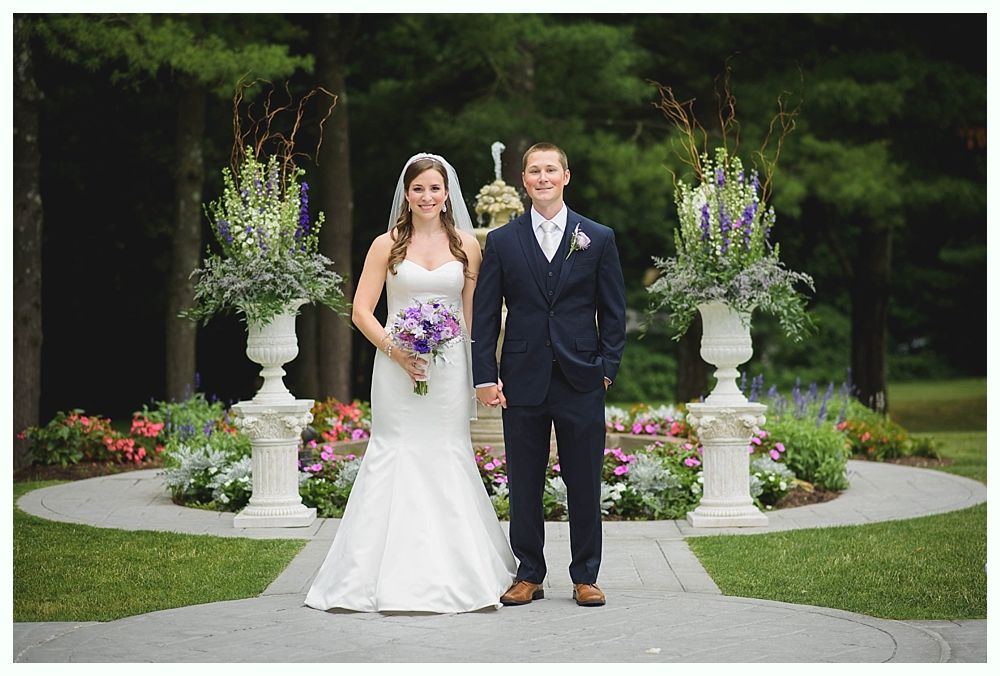 Bride with arms up, making a funny face, groom looking at his hand, cake cutting in background.