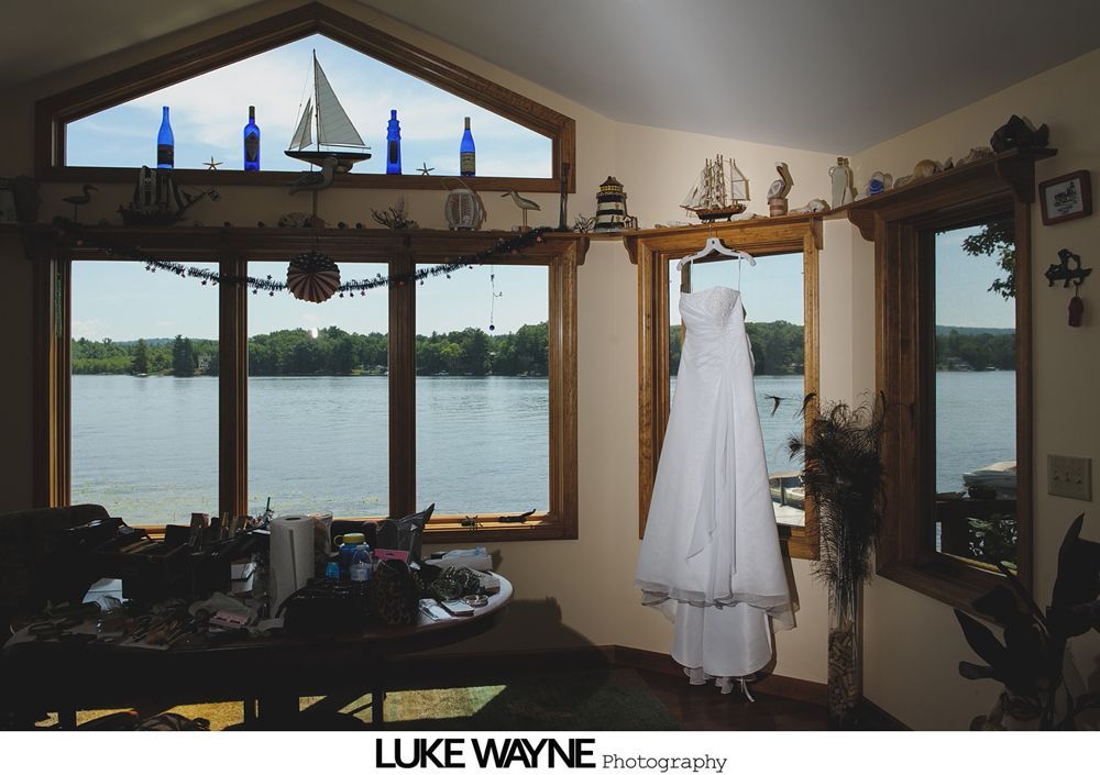 Wedding dress hanging in a room with large windows overlooking a lake.