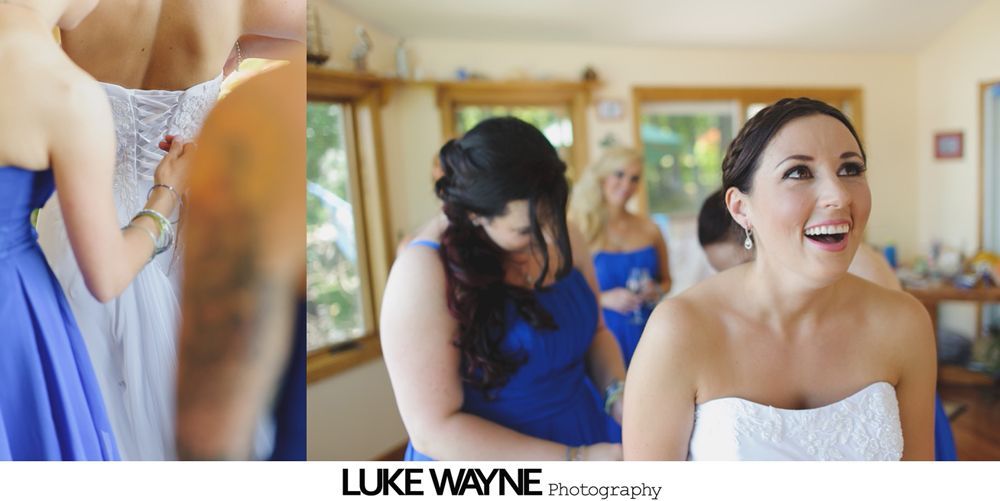 Bride smiles as bridesmaids help her into a white wedding dress. Blue dresses, a windowed room.