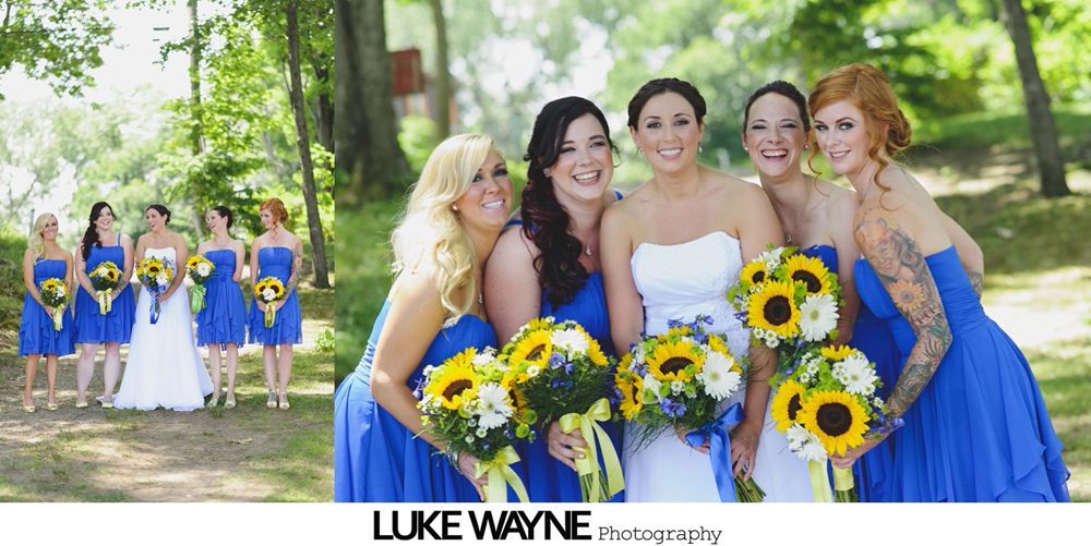 Bridesmaids in blue dresses and bride in white, smiling with bouquets of sunflowers in a green outdoor setting.