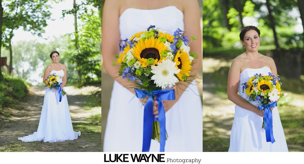 Bride in white dress holding sunflower bouquet, blue ribbon, outside, smiling.