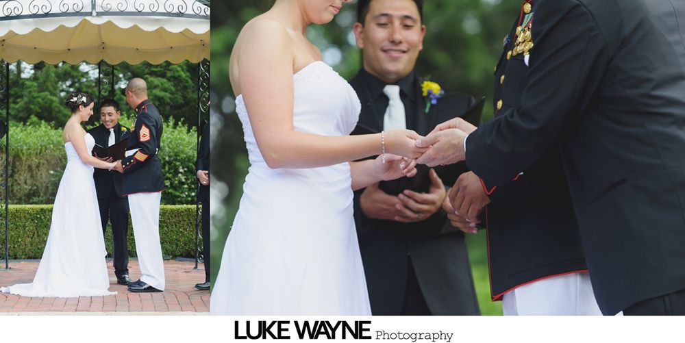 Bride and groom exchange rings at outdoor wedding ceremony. Several men in suits stand near.