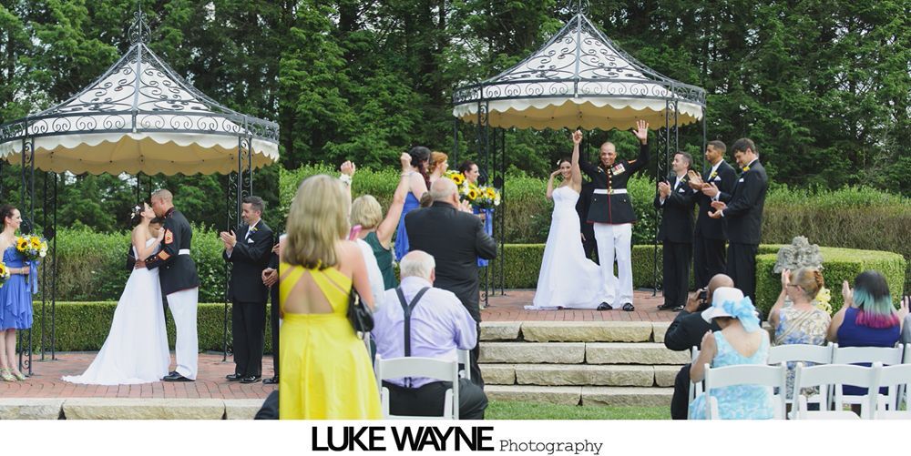 Wedding ceremony, two couples under gazebos, kissing and celebrating. Guests applaud in outdoor setting.