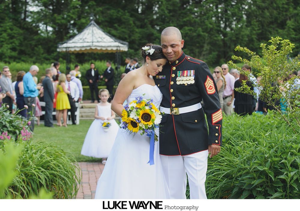 Bride and groom exiting wedding ceremony. The man is in a Marine uniform; the woman holds sunflowers.
