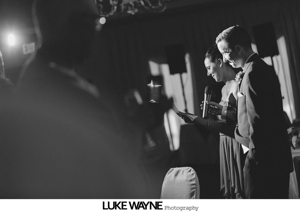 Couple reading from a tablet at a formal event, likely a wedding reception. Black and white.