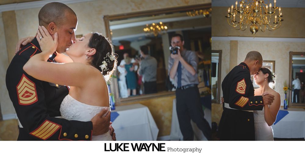 Bride and groom kissing at wedding. Marine in uniform. Photographer captures moment. Mirror reflects guests.